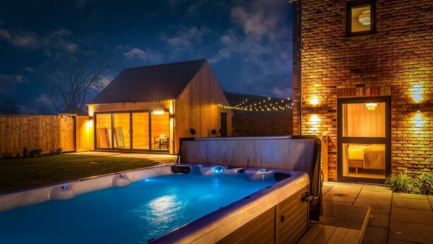 Un jacuzzi en un patio trasero con una terraza de madera y un edificio de ladrillo al fondo.