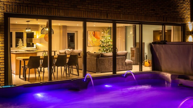 Ein moderner Poolbereich im Innenbereich mit Glaswand, einem Weihnachtsbaum und einer gemütlichen Sitzecke, die durch das Glas sichtbar ist.
