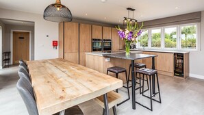 Eine moderne Küche mit Holzausstattung, einer zentralen Kochinsel, Barhocker und Pendelleuchten.