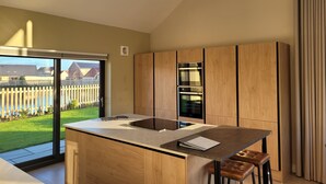 Une cuisine moderne dotée d’un grand îlot central, de meubles en bois et offrant une vue sur un jardin clos et verdoyant.