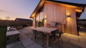 Une terrasse extérieure moderne, avec une table et des chaises en bois, un barbecue et un sapin de Noël.