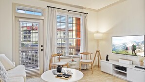 Una sala de estar moderna con un televisor de pantalla plana, una mesa de centro, dos sillones, un sofá y una ventana con persianas.