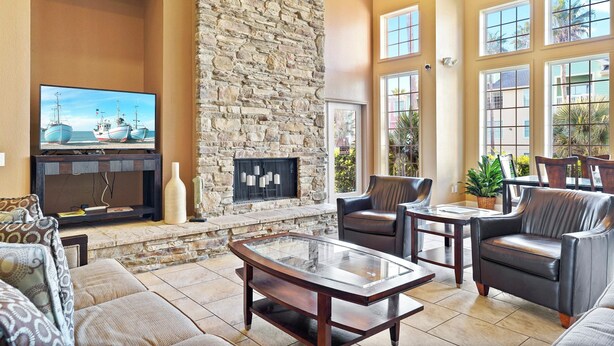 Amplia sala de estar con chimenea de piedra, asientos cómodos, televisor de pantalla plana y ventanas grandes que ofrecen vistas al exterior.