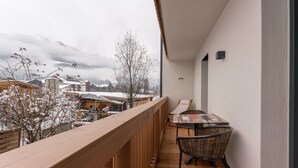 Een balkon met een houten vloer, een tafel met stoelen en een uitzicht op gebouwen en bergen op de achtergrond.