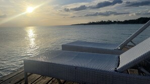 A wooden deck with a white wicker lounge chair facing a calm sea.