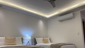 A modern hotel room with two beds, a ceiling fan, an air conditioning unit, and a bedside lamp.