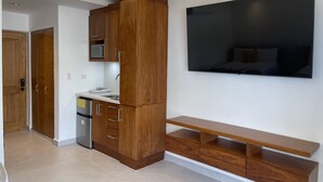 A modern kitchen with wooden cabinets, a built-in microwave, and a large flat-screen TV mounted on the wall.