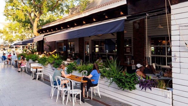 An outdoor cafe with tables and chairs, surrounded by plants and a building with a tiled roof. - South Tampa Retreat: Fenced Yard, Top Location! (Tampa)