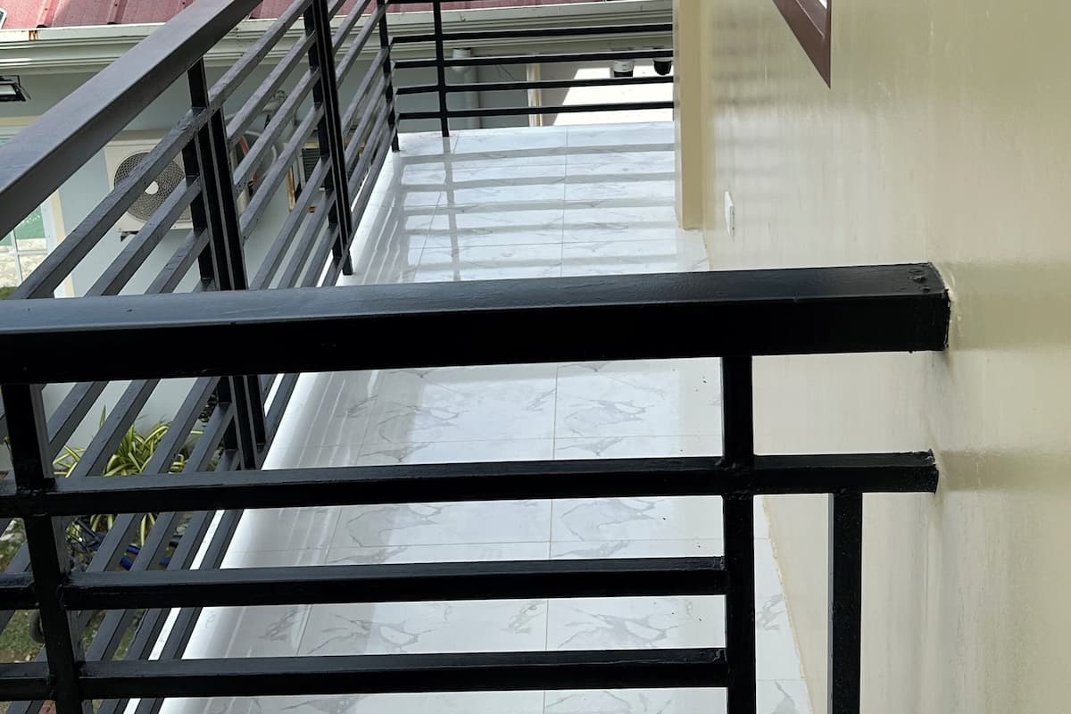 A balcony with a metal railing, a view of red-roofed buildings, and a clear sky.