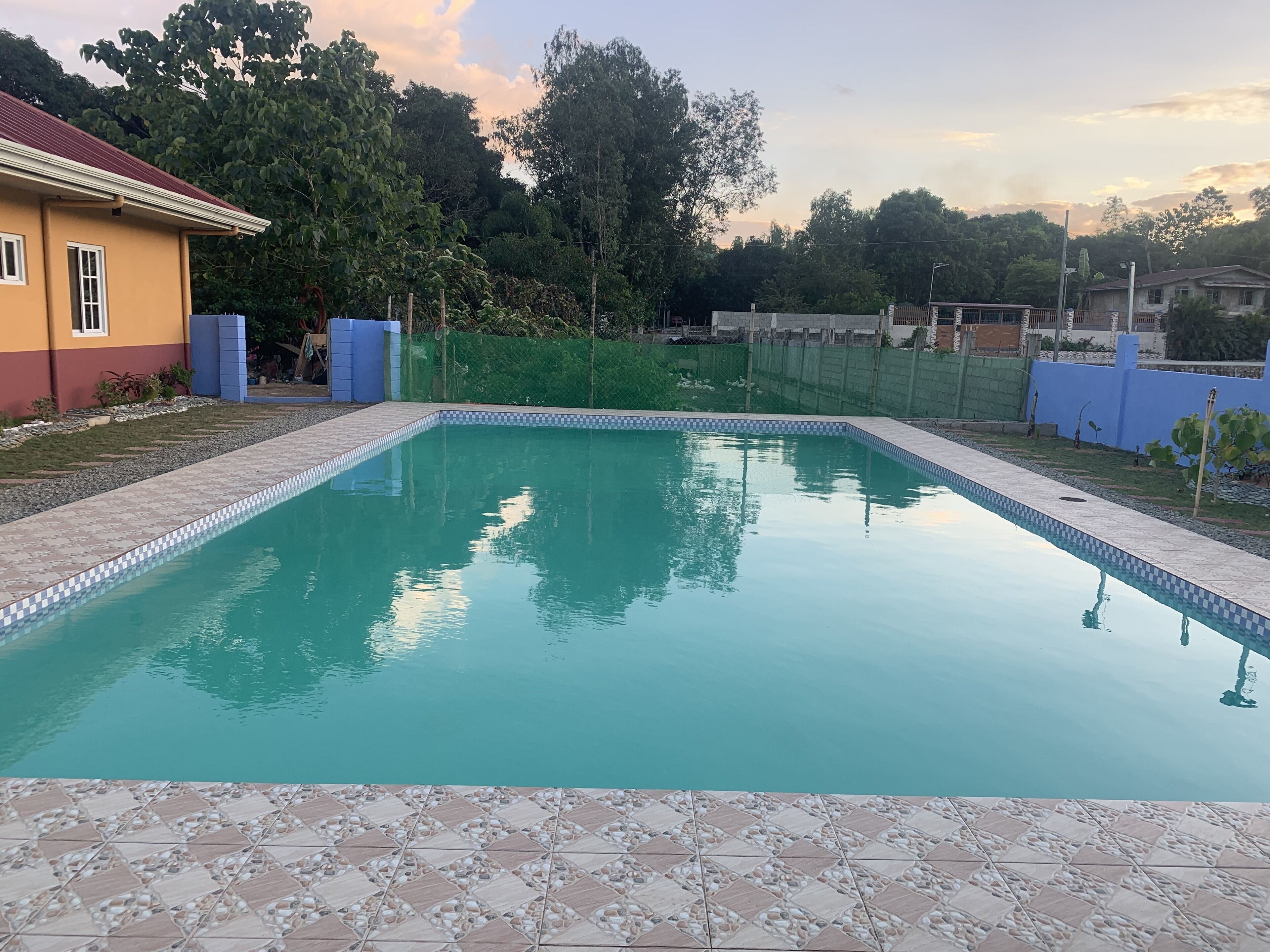 Une piscine rectangulaire dont le bord est revêtu de carreaux, entourée d’une zone pavée avec un motif de petits cailloux.