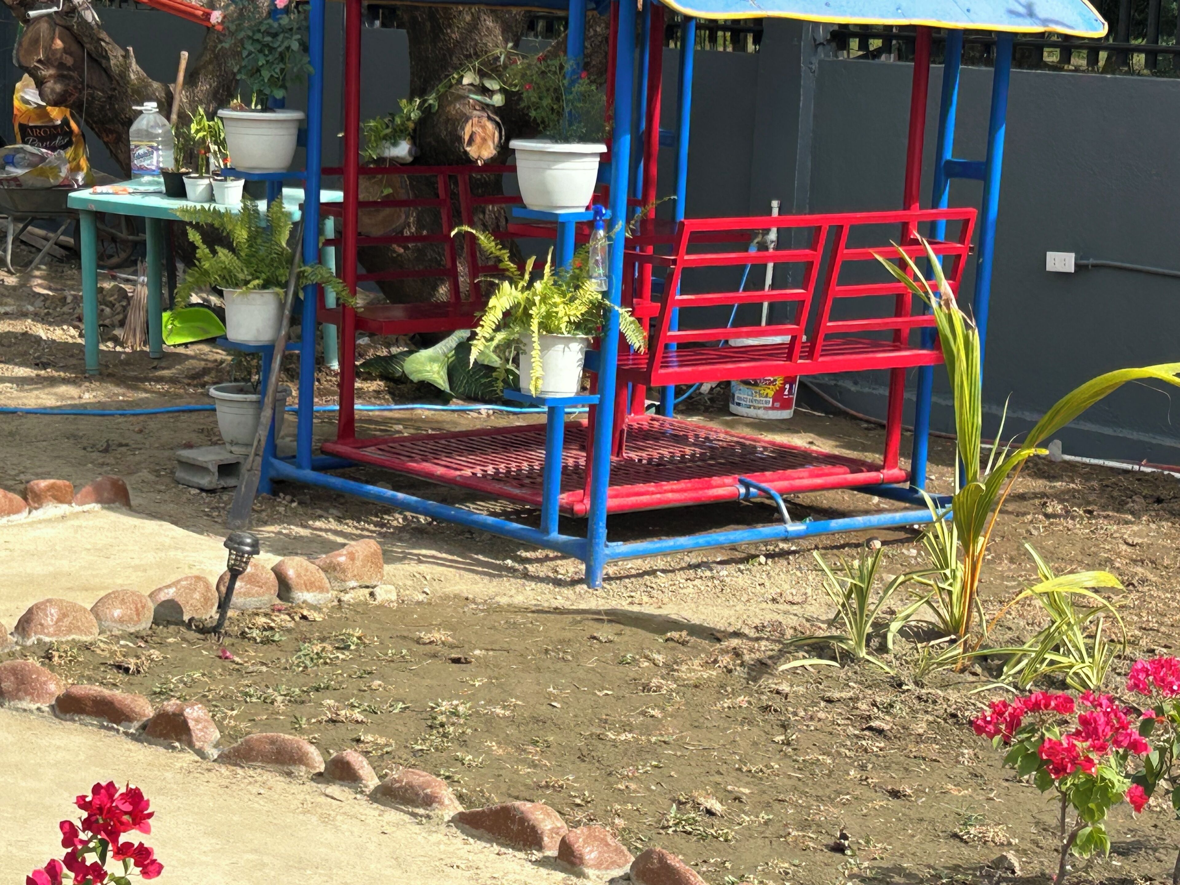 Een tuin met een rode en blauwe speelconstructie, potplanten en een kruiwagen.