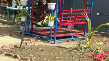Een tuin met een rode en blauwe speelconstructie, potplanten en een kruiwagen.