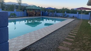 A swimming pool with a tiled deck, a wooden deck area with chairs, and a blue wall surrounding the pool. - Scarlett Resorts at Laganas  (Bugallon)