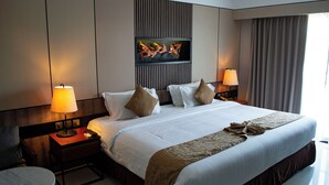 A hotel room with a large bed, two bedside tables with lamps, a small round table, and a decorative wall piece above the bed. - Scarlett Resorts at Laganas  (Bugallon)