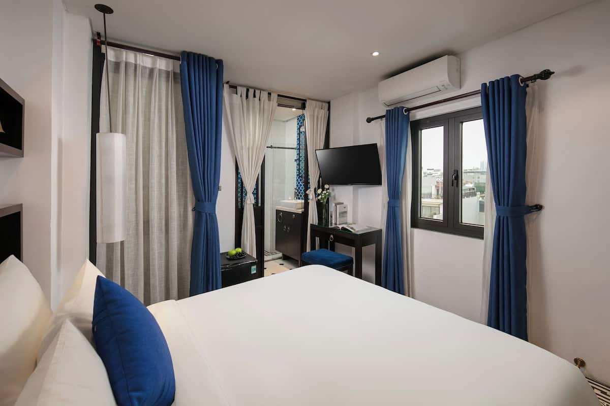 A hotel room with a bed, a desk, a TV, and a window with curtains.