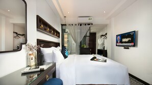 A hotel room with a large bed, a desk with a mirror, a television on the wall, and a patterned floor. - Carillon Boutique Hotel (Hanoi)