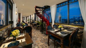 A restaurant with a spiral staircase, marble flooring, and large windows offering a city view. - Carillon Boutique Hotel (Hanoi)