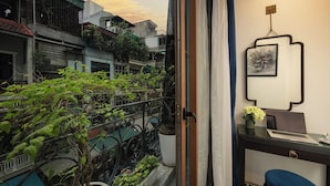 A room with a view of a courtyard, a desk with a laptop, a vase with flowers, and a framed picture on the wall. - Carillon Boutique Hotel (Hanoi)