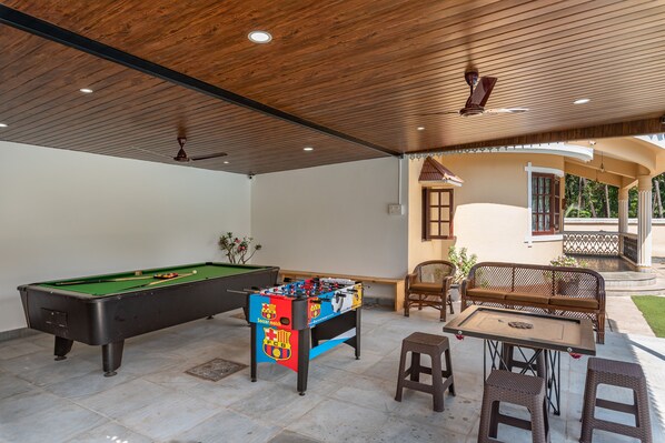 A pool table, a foosball table, and a table with chairs in a covered outdoor area.
