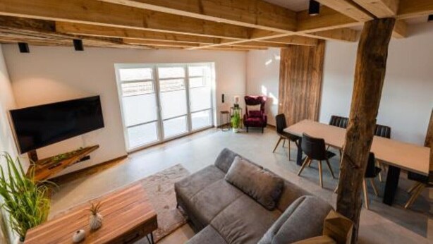 A spacious living area with a large sofa, a dining table, and a TV mounted on the wall.