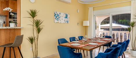 A dining area with a long table, blue chairs, and potted plants.