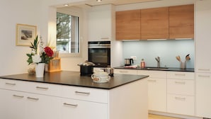 A modern kitchen with white cabinetry, a central island, and a window providing natural light. - Grillon by Interhome (Zermatt)