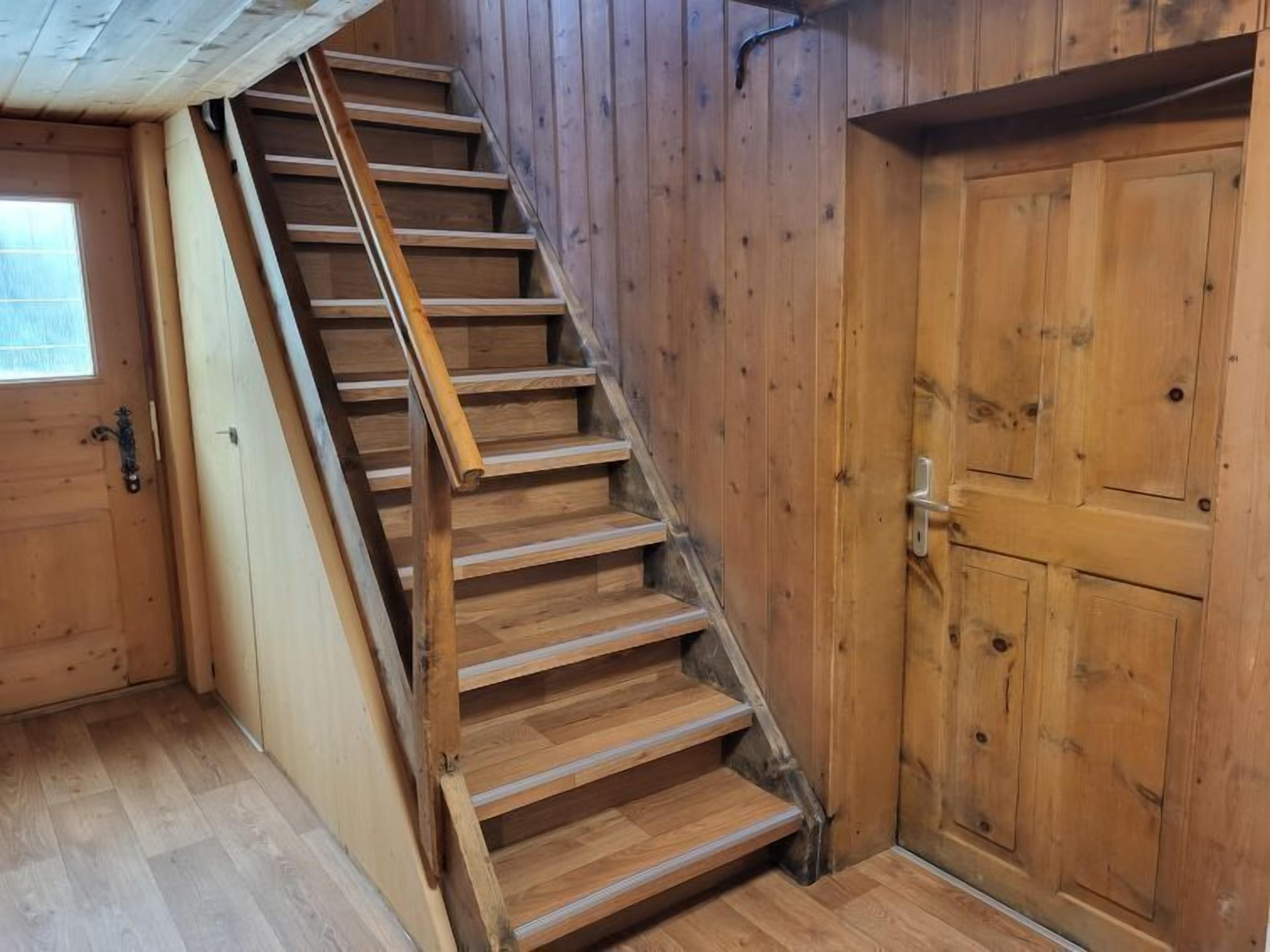 Een houten trap met een leuning die naar een deur met een metalen handgreep leidt.