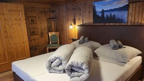 A wooden cabin bedroom with a bed, pillows, a chair, and a painting of a mountain landscape.