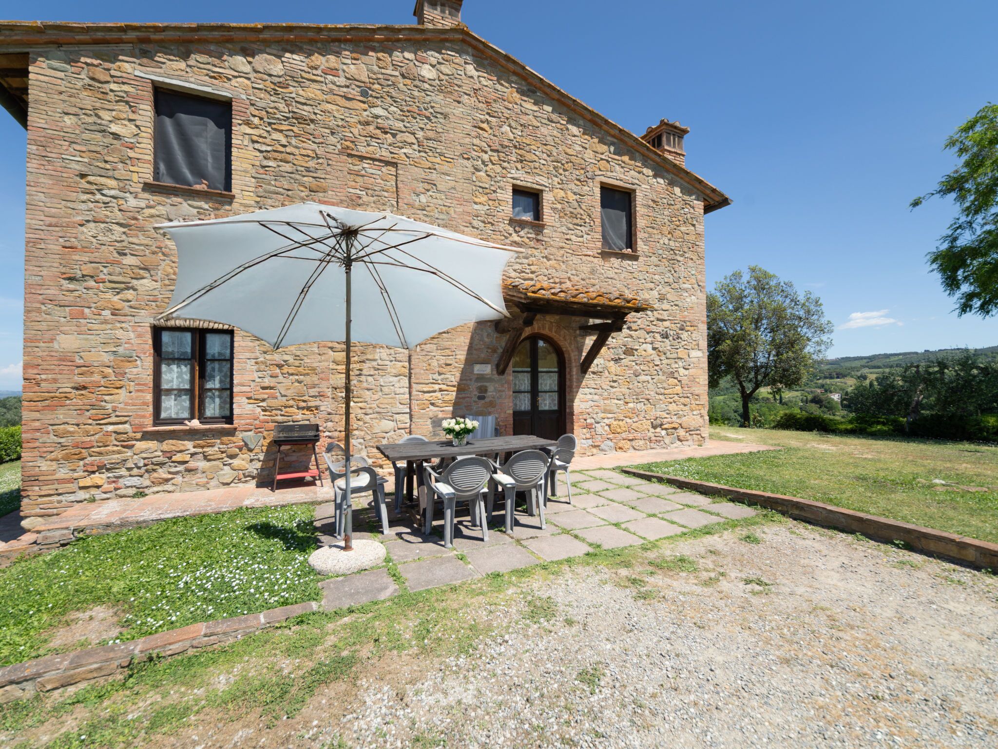 Un bâtiment en pierre doté d’un patio comprenant une table, des chaises, un parasol et un barbecue.