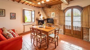 A cozy dining area with a wooden table and chairs, a fireplace, and a stone wall. - Baccelli by Interhome (Montaione)