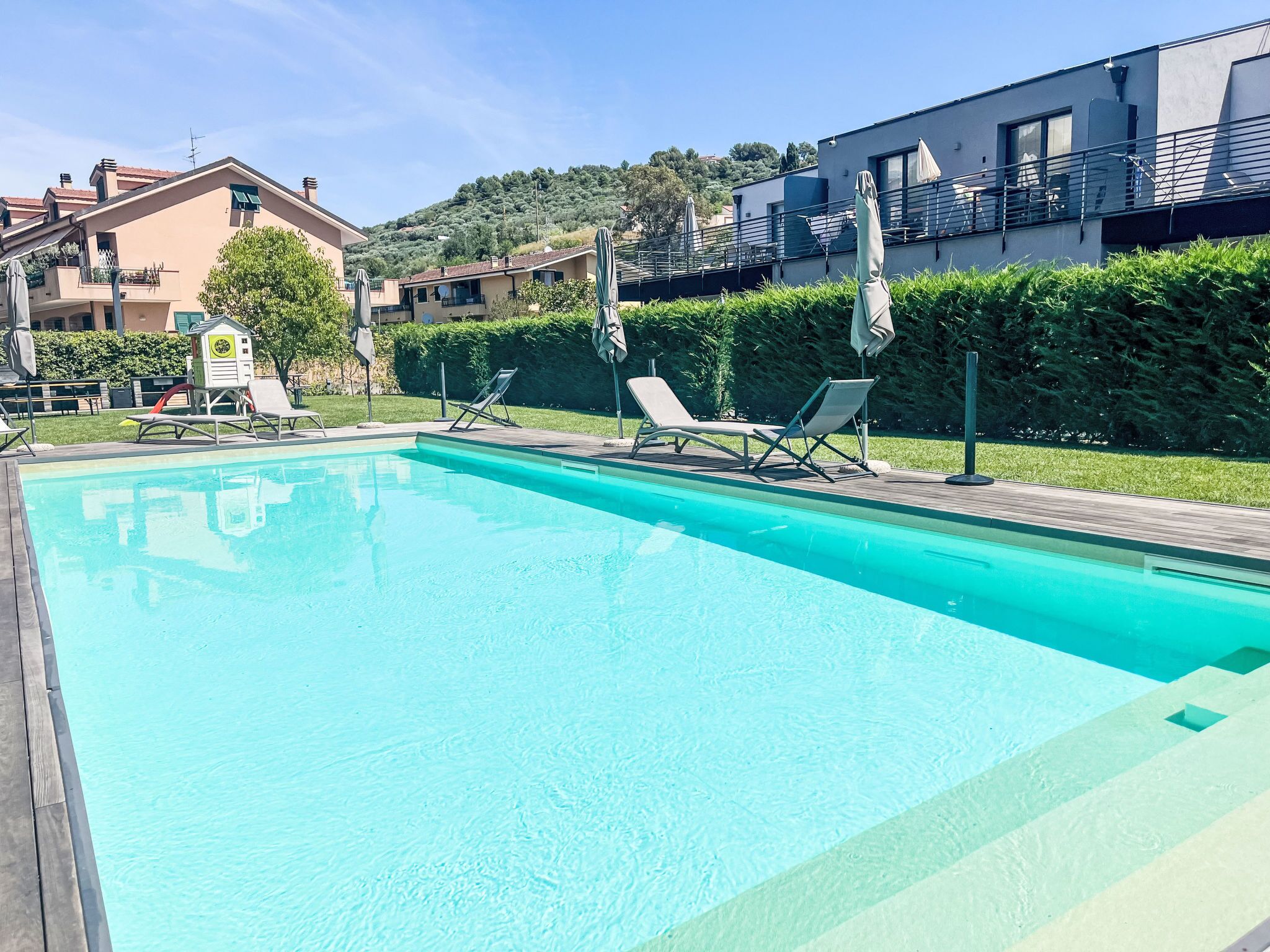 A swimming pool with lounge chairs, a lifeguard tower, and a view of residential buildings.
