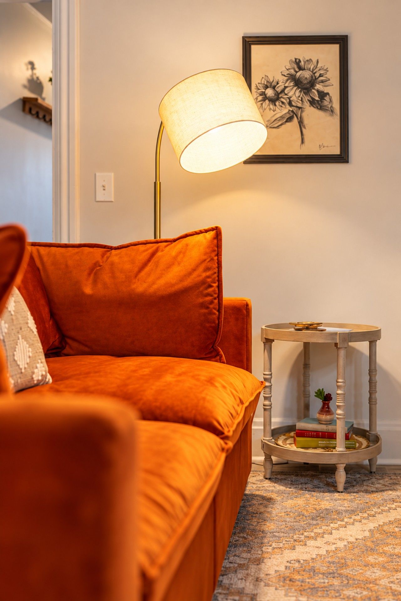 A room with a sofa, a lamp, a small table with books, and a framed artwork on the wall.