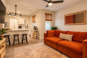 A living room with a sofa, a coffee table, and a dining area with a kitchen in the background. - 307 37th St · Sauna, King Bed, Walkable | Lawrenceville Row Home (Pittsburgh)