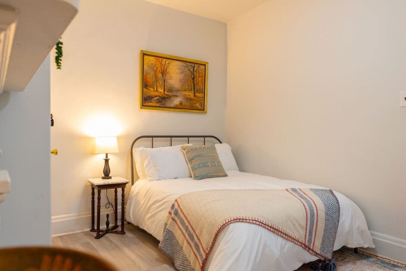 Un dormitorio con una cama, una mesita de noche con lámpara, un cuadro en la pared y una alfombra pequeña.
