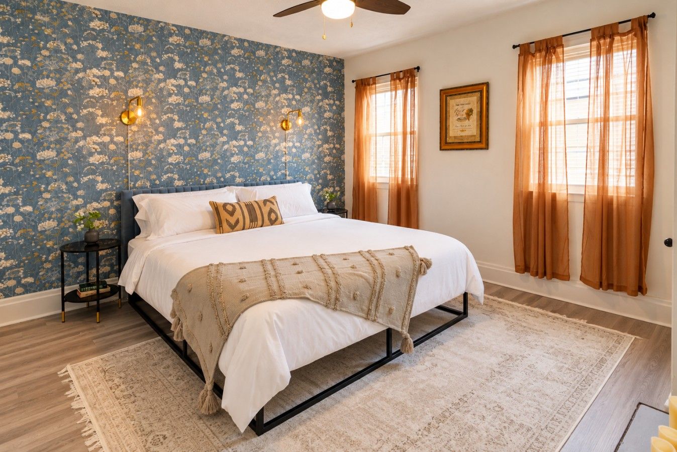 A bedroom with a bed, a nightstand, a wall-mounted light fixture, and a window with curtains.