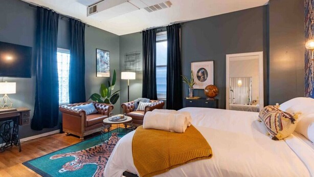 Une chambre d’hôtel avec un grand lit, deux fauteuils, une table basse, un bureau et une grande fenêtre.