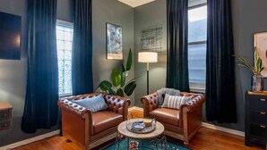 Un salon avec deux canapés en cuir, une table basse, un lampadaire et une grande fenêtre avec des rideaux.