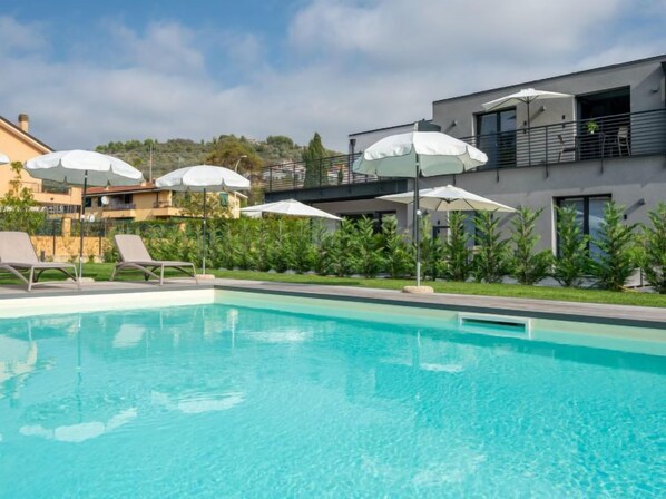 Ein Schwimmbad mit Liegestühlen und Sonnenschirmen, umgeben von Grünflächen und modernen Gebäuden.