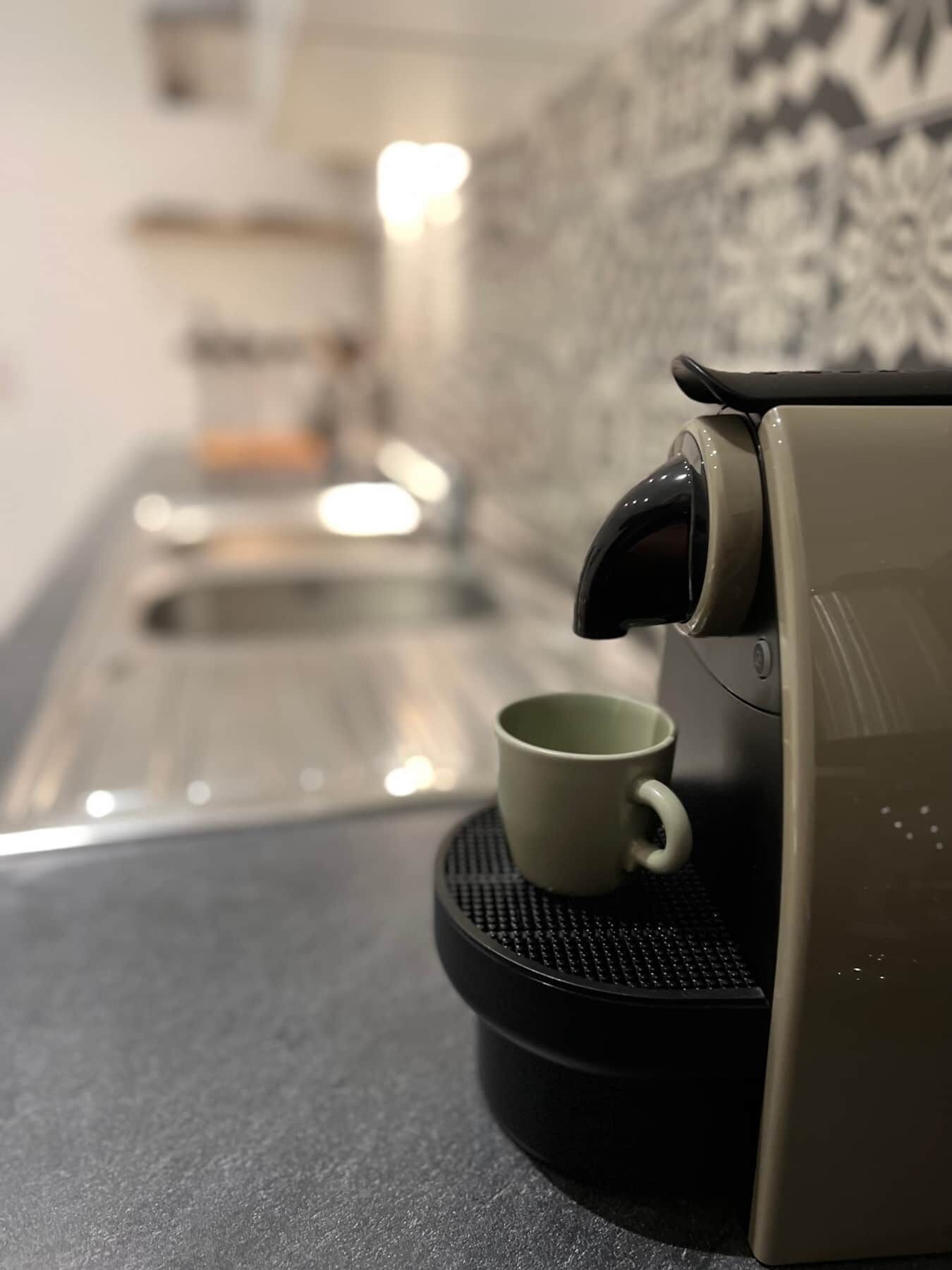 A coffee machine with a cup on a coaster, a sink, and a patterned backsplash.
