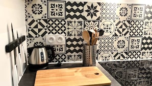 Una cocina con baldosas estampadas, una tetera, una tabla de cortar y utensilios.
