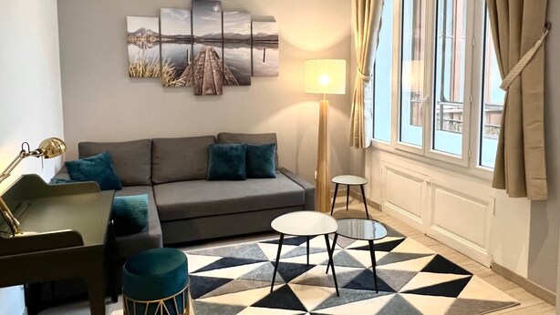 Una sala de estar con un sofá, dos mesitas, una lámpara y un tapete de estampado geométrico.