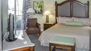 A hotel room with a bed, a chair, a desk with a television, and a window with a view of greenery.