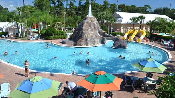 A swimming pool with a water slide and a rock formation, surrounded by umbrellas and lounge chairs.