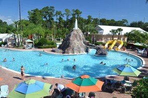 Ein Swimmingpool mit Wasserrutsche und Felsformation, umgeben von Sonnenschirmen und Liegestühlen.