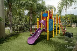 A playground with a purple slide, yellow and red play structures, and a black bench.