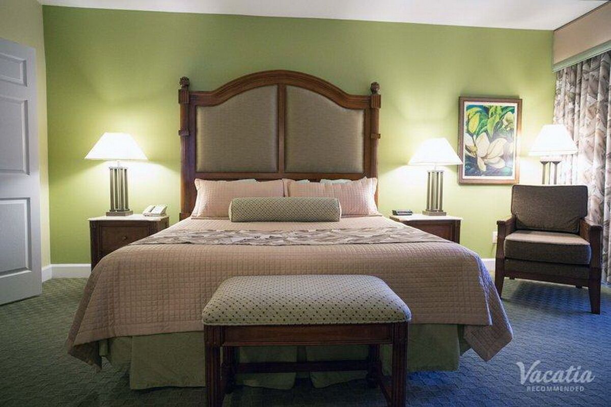 A hotel room with a large bed, two bedside lamps, a chair, and a painting on the wall.