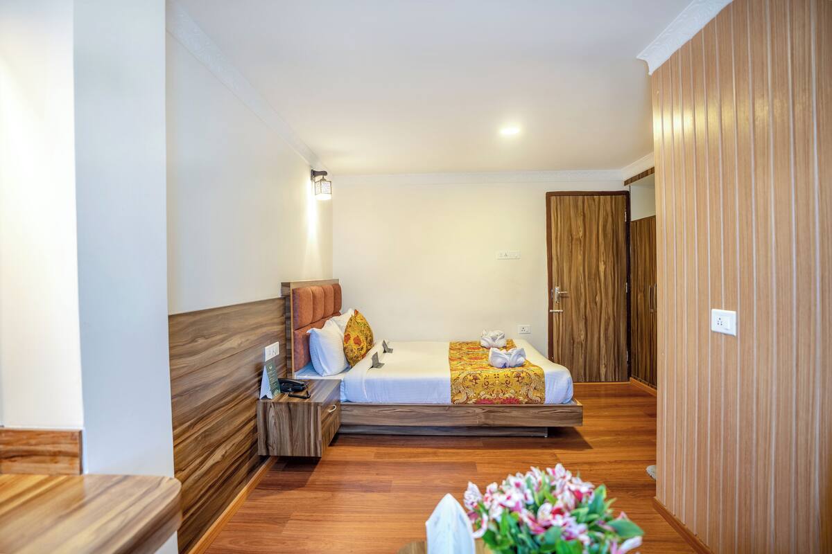 Ein Hotelzimmer mit einem Holzbett, einem Nachttisch, einem Beistelltisch und einem kleinen Tisch mit Blumen.