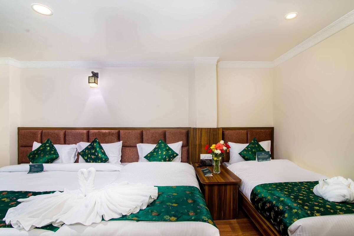 Ein Hotelzimmer mit zwei Betten, einem Holzkopfteil und einem Nachttisch mit Blumen in einer Vase.