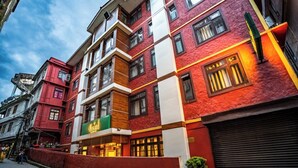 A multi-story hotel with a red facade, multiple windows, and a visible restaurant sign. - Muscatel Dzeemkhang (Gangtok)