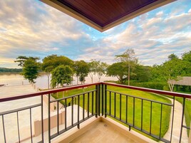 Un balcón con vista a un río y árboles, techo de madera y barandilla roja.